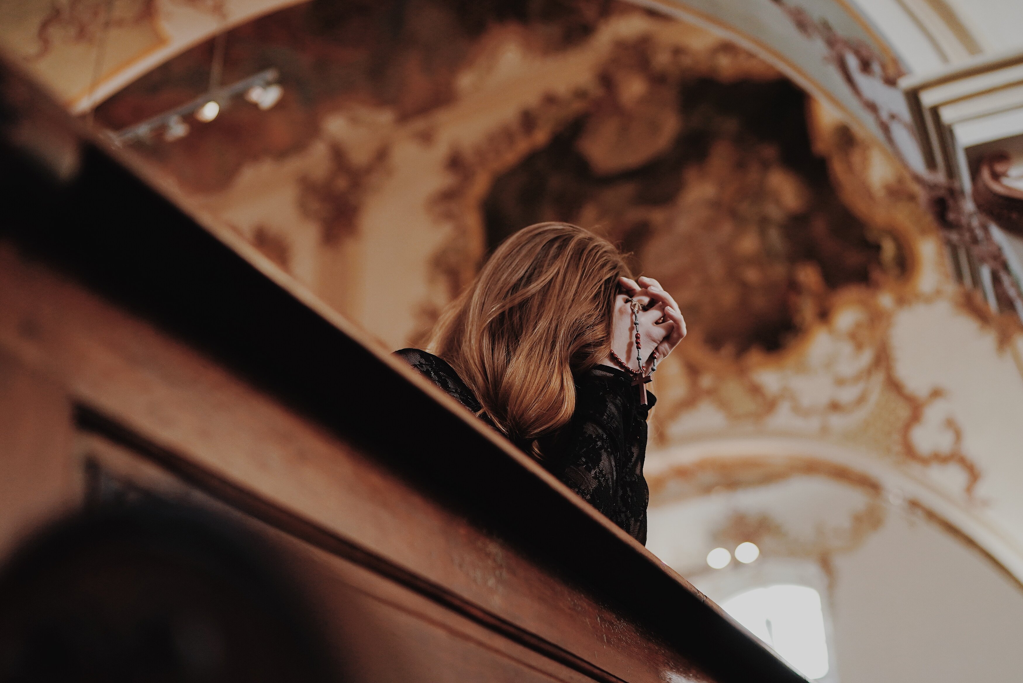 Blick auf eine junge Frau, die den Rosenkranz betet. Im Hintergrund ist die Decke der Kapelle zu sehen.