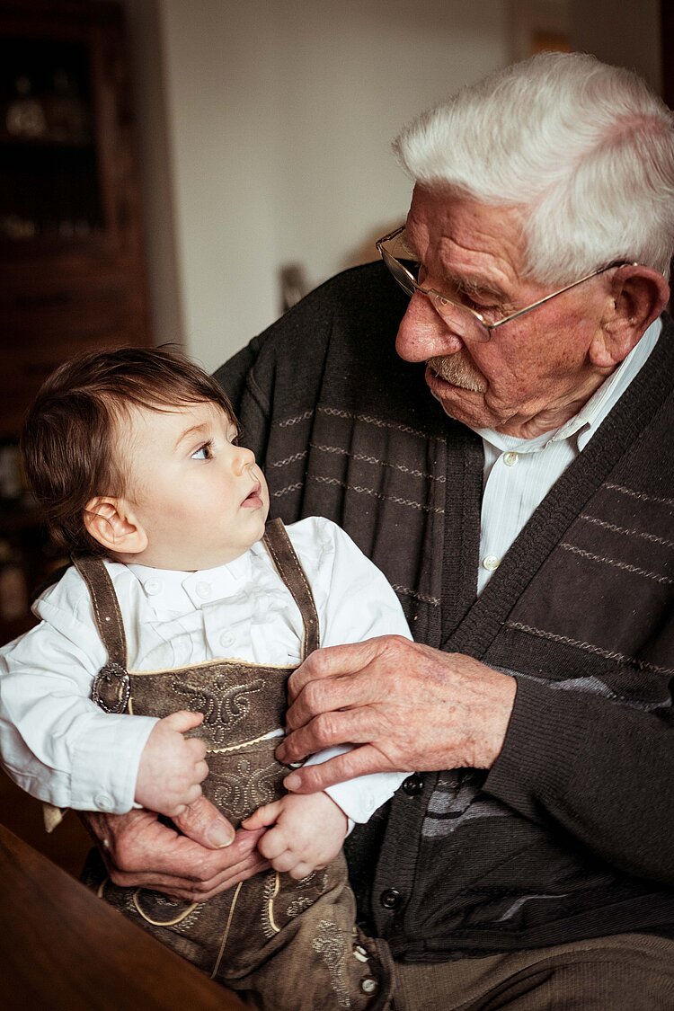 Ein älterer Herr mit einem kleinen Jungen auf dem Arm, die sich gegenseitig ansehen.